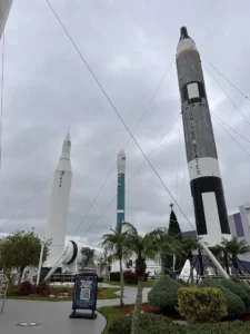 Tres cohetes parados en un cielo nublado. El primero es todo blanco, el segundo verde con la punta redonda y la cara de un tiburón pintado y el tercero es gris con la punta negra y blanca