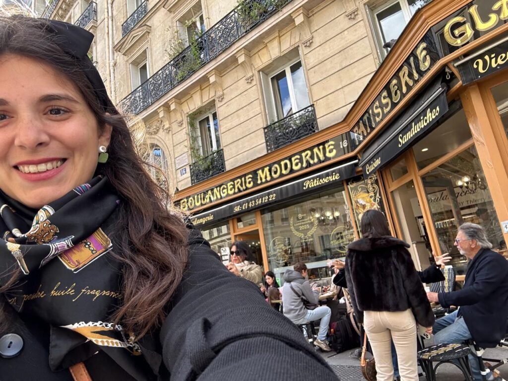 Selfie en frente de la Boulangerie Moderne en París, destacando la típica atmósfera de cafetería francesa con su decoración clásica, invitando a los transeúntes a disfrutar de un croissant y un café.