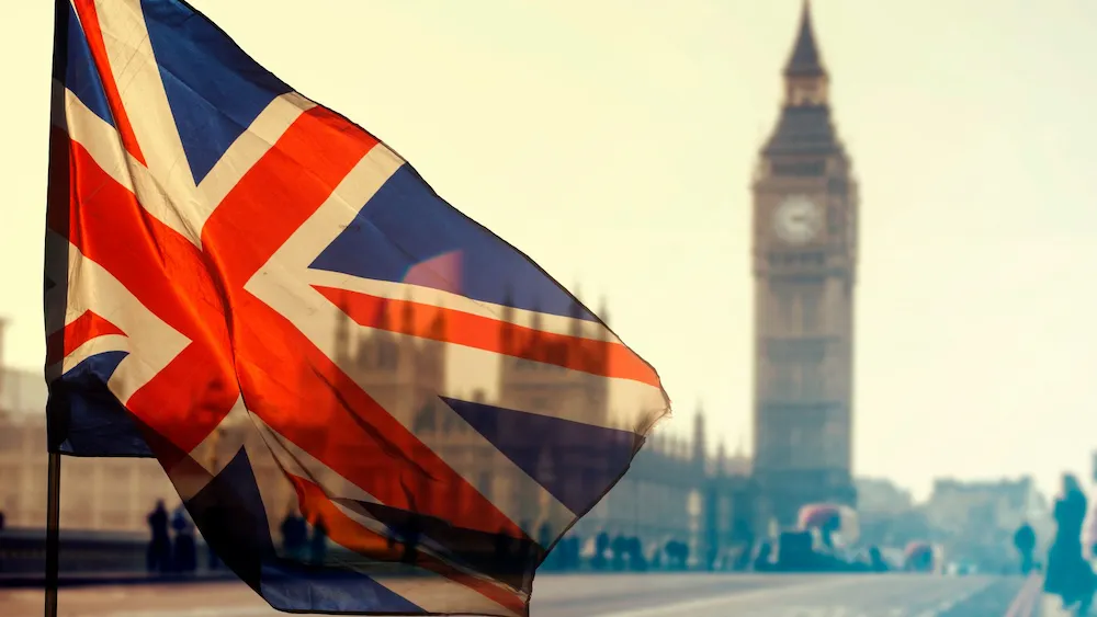 Bandera del Reino Unido ondeando con el icónico Big Ben desenfocado al fondo, en una escena típica de Londres al atardecer