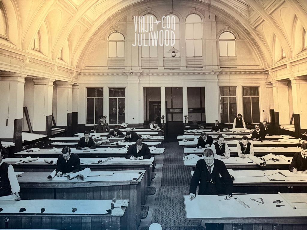 Fotografía antigua de una sala de diseño naval con arquitectos trabajando en planos del Titanic en mesas largas.