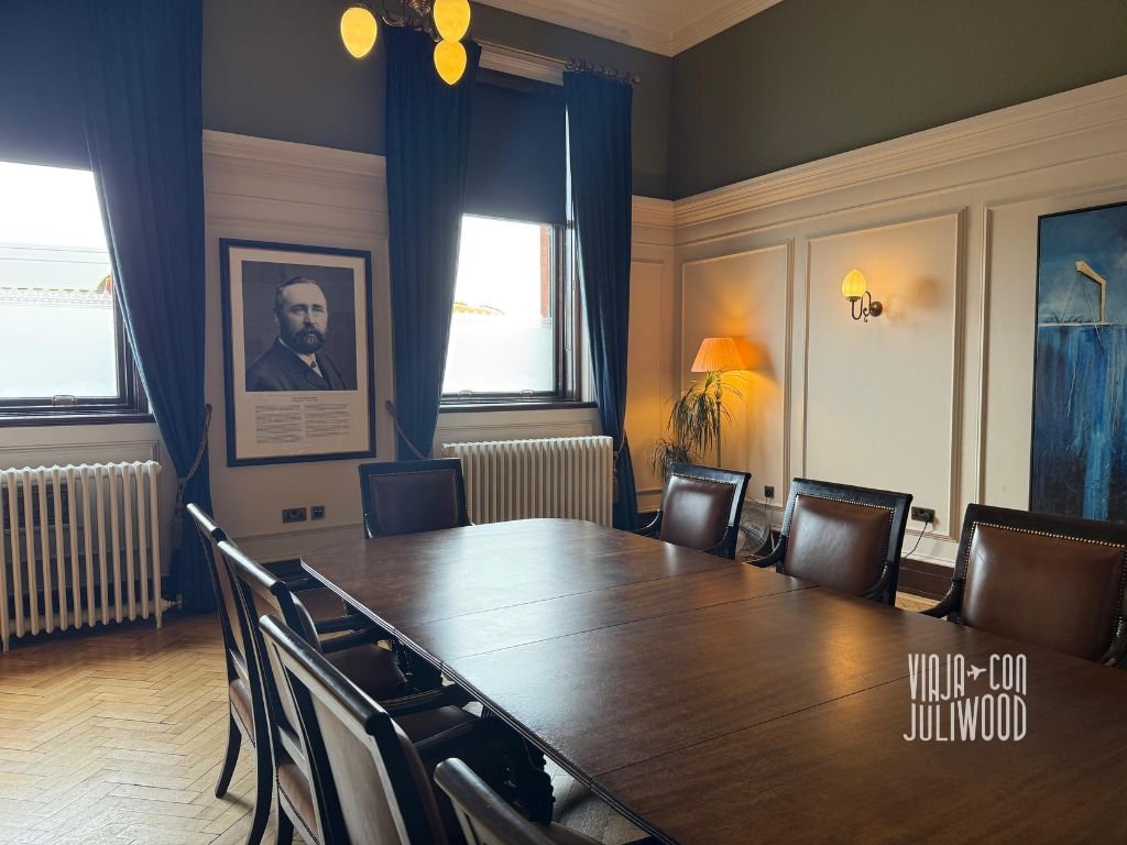 Elegante sala de reuniones con mesa de madera, retrato en la pared y cortinas azules, dentro del museo Titanic Belfast.