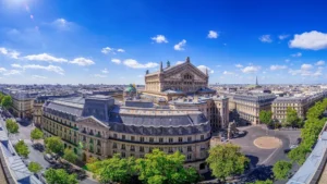 Vista panorámica de la ciudad de París desde un punto alto, con la majestuosa Ópera Garnier en el centro y la Torre Eiffel al fondo bajo un cielo azul brillante.