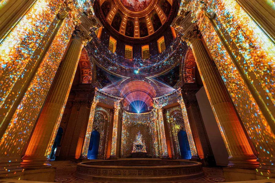Espectáculo de luces AURA en la cúpula de Les Invalides, París, donde proyecciones multicolores iluminan columnas y bóvedas históricas.