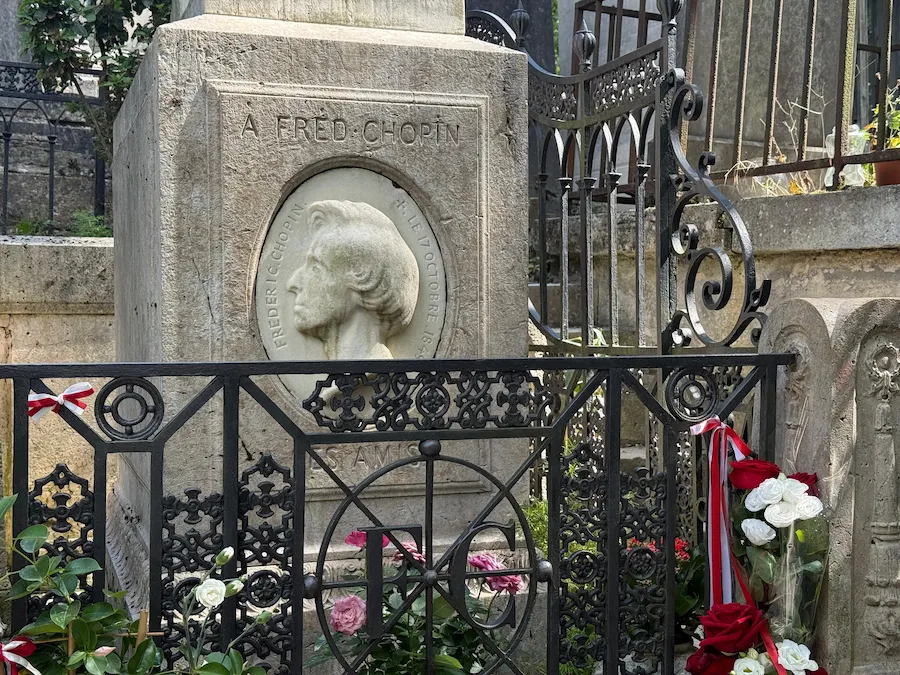 Tumba de Frédéric Chopin en el cementerio Père-Lachaise de París, rodeada de flores y cintas polacas que homenajean al compositor.