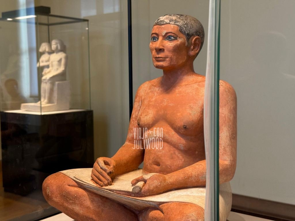 Estatua egipcia del Escriba Sentado en el Louvre, figura de un escriba con ojos incrustados y rasgos detallados sosteniendo un rollo.
