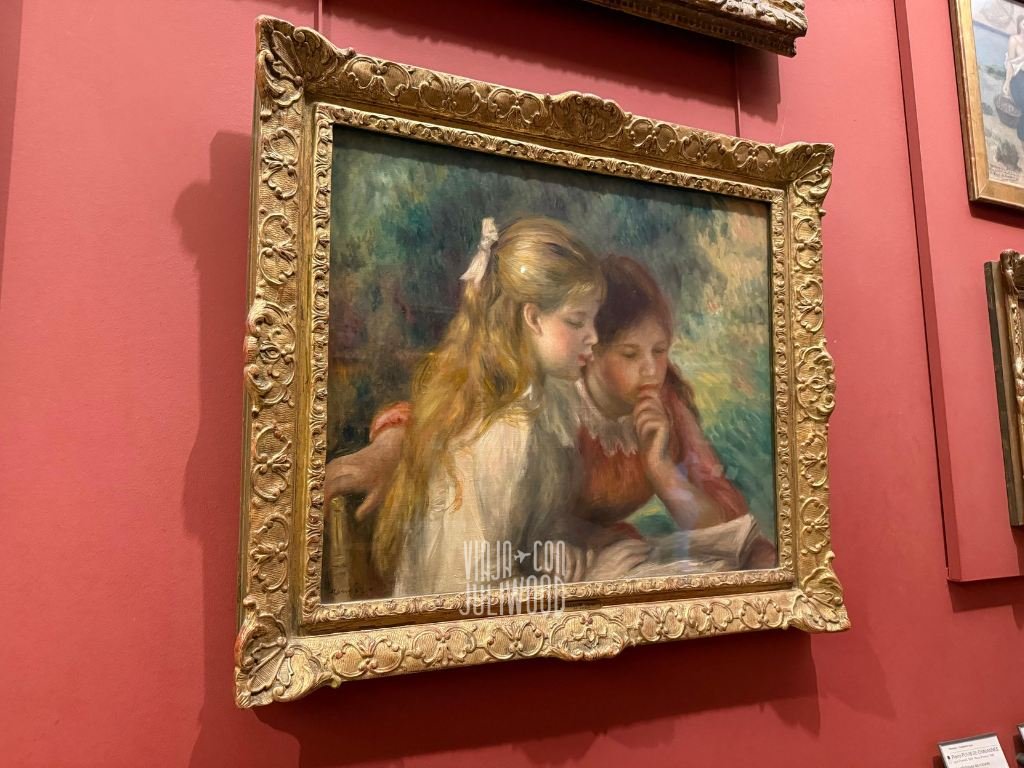 Pintura impresionista de Renoir en el Louvre que muestra a dos niñas leyendo juntas, con suaves pinceladas y tonos cálidos.