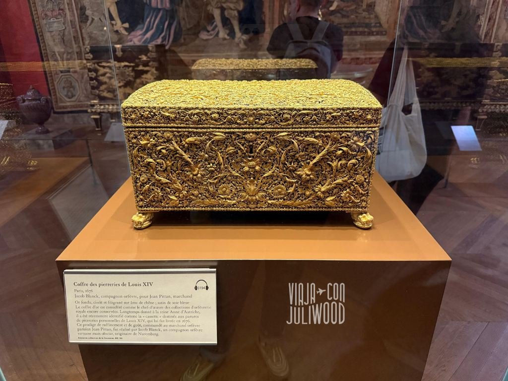 Cofre dorado de Louis XIV expuesto en el Louvre, una caja ricamente ornamentada con filigranas y relieves detallados en oro sobre un pedestal en vitrina.