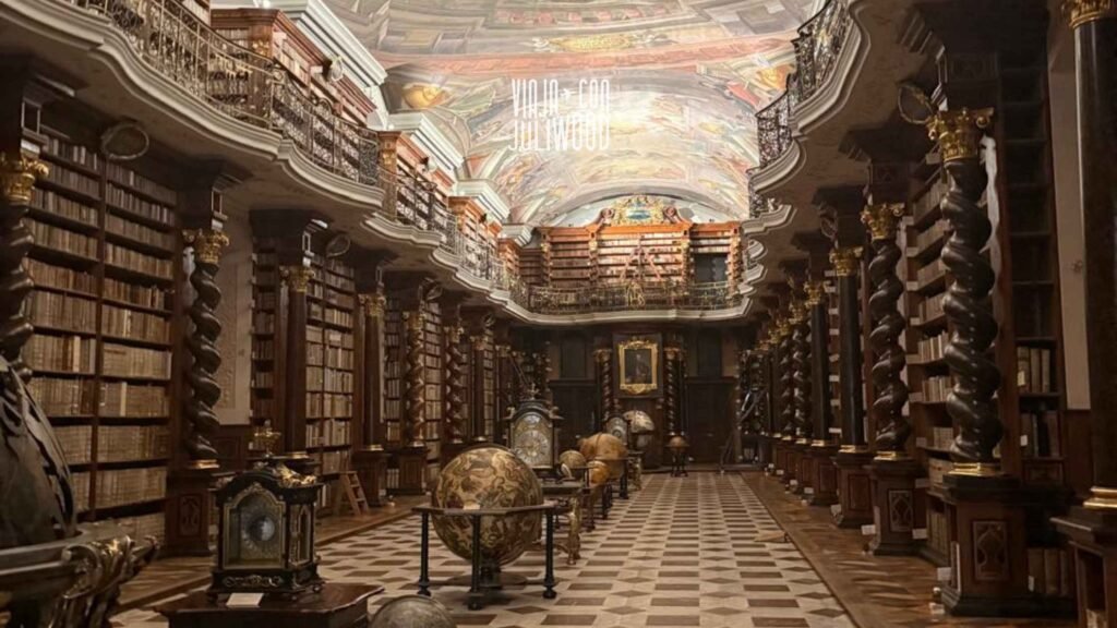 Biblioteca barroca del Klementinum con estanterías de madera, globos antiguos y frescos en el techo.