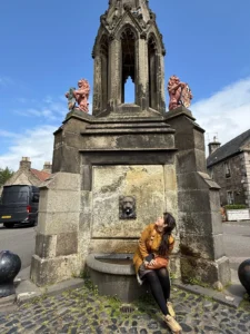 Juli sentada junto a la fuente Bruce Fountain en Falkland, donde se filmó la escena del misterioso escocés en Outlander.